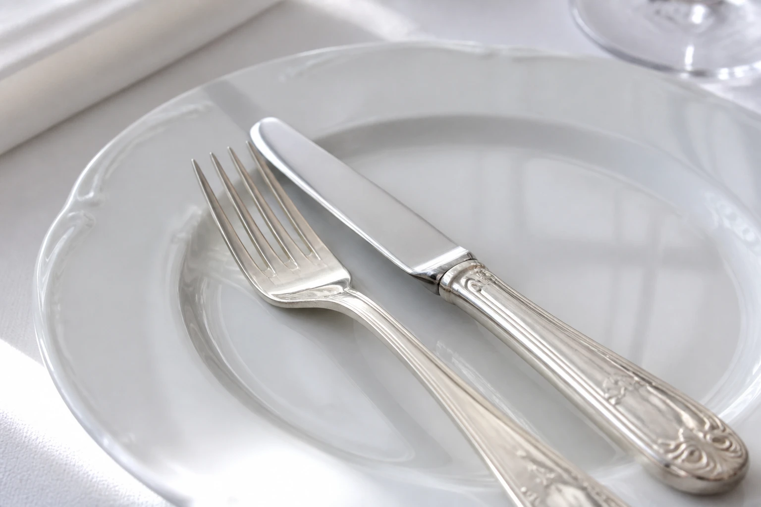 Fourchette et couteau posés en position 16h20 dans une assiette blanche sur nappe de lin